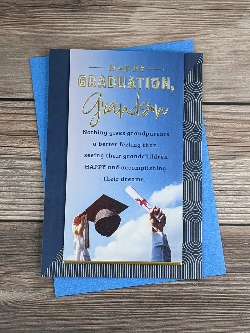 A blue graduation greeting card for a grandson, with an image of arms reaching up to the sky holding a grad cap and a diploma.