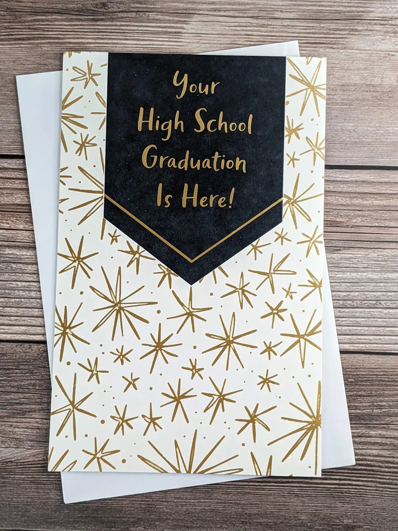An American Greetings graduation card with a white cover that has a design of gold stars.