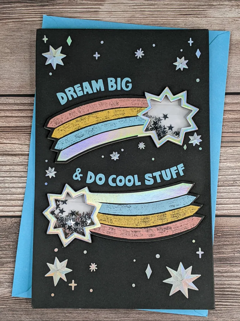 A graduation card with a black cover, a design with dimensional shooting stars that contain shakable confetti of silver stars.