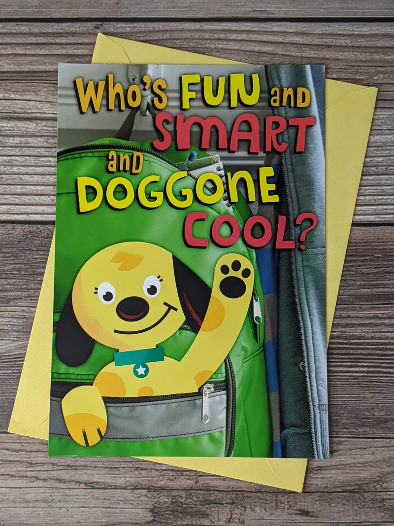 A starting school greeting card with an image of a dog waving from the pocket of a backpack on the cover.