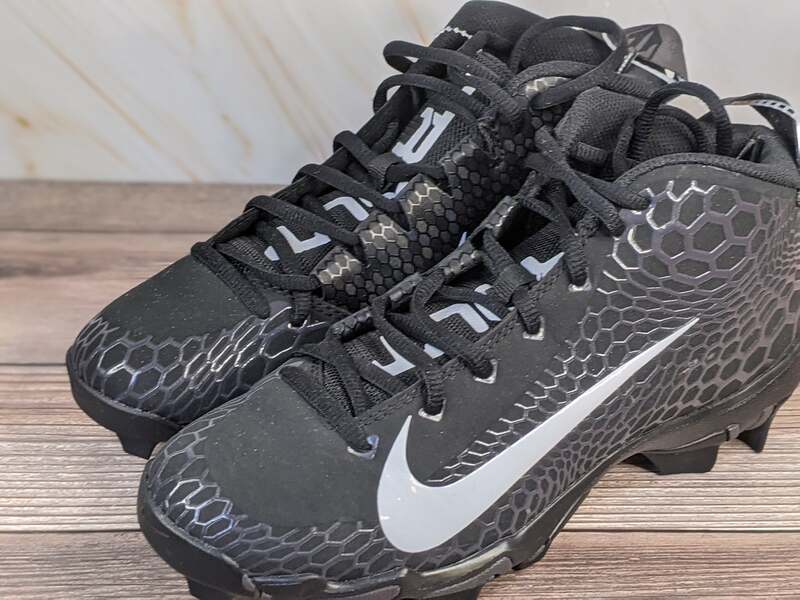 A pair of black cleats for youth by Nike Trout Fastflex, with a white swoosh and black laces.