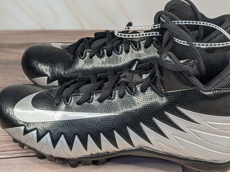 Nike Youth football cleats that are black with silver shark-patterned accents.