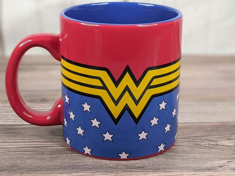 A ceramic mug that has a blue, red and yellow Wonder Woman logo with a pattern of white stars.